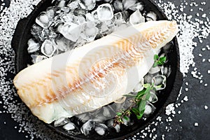 Fillet of white sea cold-water fish cod in ice cubes on a dark background. Top view