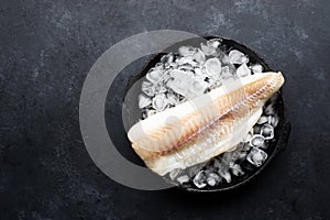 Fillet of white sea cold-water fish cod in ice cubes on a dark background. Top view