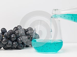 Filling a glass glass with an exotic cocktail on a background of blue grapes