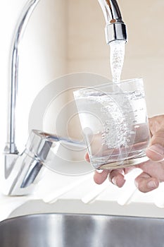 Filling glass of water in hand from kitchen faucet photo
