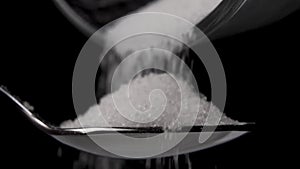 Filling a metal shiny spoon with granulated sugar from a metal container on a black background.