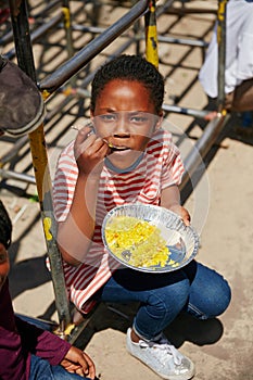 Filling my tummy with food. Full length portrait of a young girl getting fed at a food outreach.