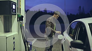 Filling station. A man fills his car with gasoline at night