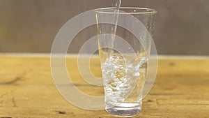 Filling a transparent glass with cold water in the kitchen on the wooden table. water is poured into glass beaker.