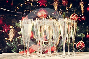 Filling up glasses for party. Glasses of champagne with Christmas tree background. Holiday season background. Traditional red and
