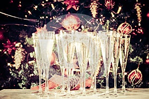 Filling up glasses for party. Glasses of champagne with Christmas tree background and sparkles. Holiday season background.