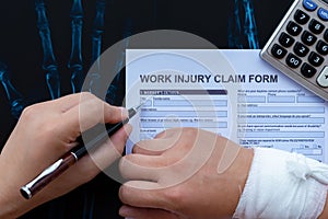 Filling up a work injury claim form with a wrapped hand on top of an X-ray film