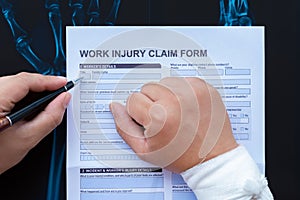 Filling up a work injury claim form with a wrapped hand on top of X-ray film medical and insurance concept