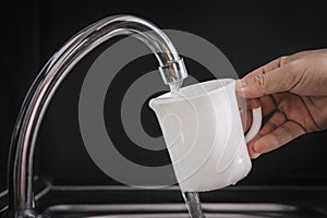 Filling white glass with tap water. Modern faucet and sink in home kitchen. pouring fresh drink cup on black background, housework