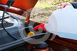 Filling windshield washer fluid in car. Driver with washer fluid in his hands, close up. Car maintenance concept