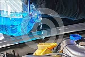 Filling a windshield washer tank of a car with a wiper fluid outdoors