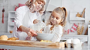 Fills with milk. Senior grandmother with her little granddaughter cooks sweets for Christmas on the kitchen