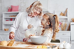 Fills with milk. Senior grandmother with her little granddaughter cooks sweets for Christmas on the kitchen