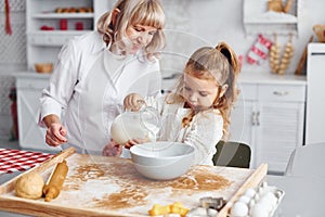 Fills with milk. Senior grandmother with her little granddaughter cooks sweets for Christmas on the kitchen