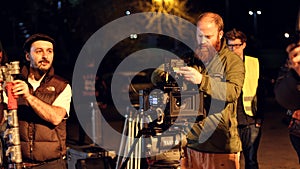 Film crew on location, night shoot. Cinamatographer with 4k camera