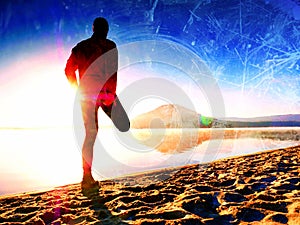 Film effect. Man exercising on the beach. Silhouette of active man exercising and stretching on the lake beach at sunrise.