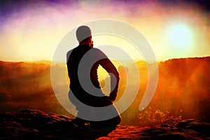 Film grain. Sportsmann hiker in black sportswear sit on mountain top and take a rest with watching down to morning valley.