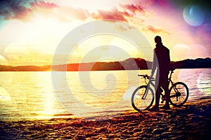 Film grain. Young man cyclist silhouette on blue sky and sunset background on the beach. End of season at lake.