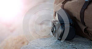 The film medium format camera lies on the stones against the backdrop of a canvas vintage backpack. In the sun