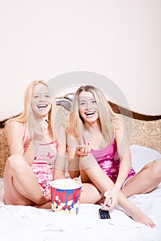 Film time: Two girl friends or sisters blond adorable attractive pretty young women sitting in bed with popcorn, watching movie