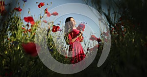 Filming from below of young brunette woman in a red polka dot dress walks with bouquet in the middle of the field of