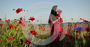 Filming from below of young brunette woman in a red polka dot dress walks with bouquet in the middle of the field of