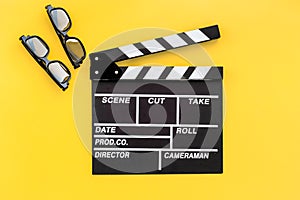 Filmmaker accessories. Clapperboard and glasses on yellow background top view