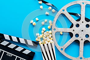 Filmmaker profession with clapperboard, popcorn and video tape on blue background top view copyspace