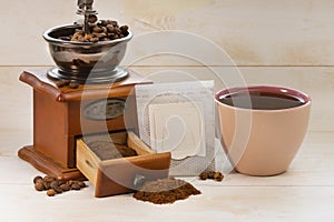 Filter bag with ground coffee, manual coffee grinder and cup of espresso coffee on a white isolated background. Copy space