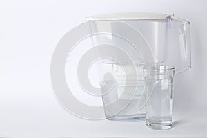 Filter jug and glass with purified water on white background. Space for text