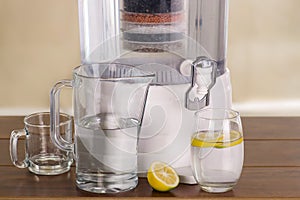 Filter system of water purifier with two glasses of water one filled until middle with a lemon inside and an empty