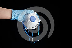 Filtering facepiece respirator in hand in blue glove, isolated on black background