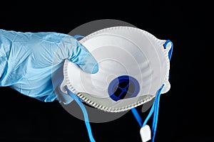 Filtering facepiece respirator in hand in blue glove, isolated on black background