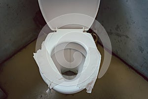Filthy toilet seat covered with toilet paper as sit down insulation