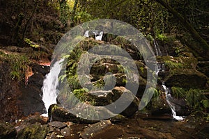 Filveda waterfall through green vegetation and red stones photo