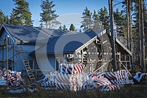 The final stage of construction of a large, gray, frame country house in a pine forest a