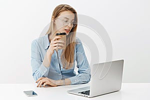 Finance, business and work concept. Attractive female businesswoman with fair hair in glasses drinking coffee, working