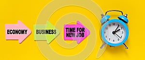 On a yellow background, a blue alarm clock, and paper arrows. On the pink arrow it says - Economy, on the yellow - Business and on