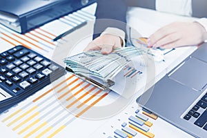 Finance. Female hand with money stack and calculator on financial graphs on desk