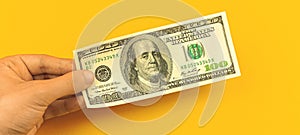 Finance investment concept, man hand hold one banknote, one hundred dollar bill on a yellow background of business