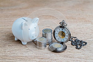 Finance or long term saving money and investment concept, white piggy bank and coins stacked and pocket watch on wood table