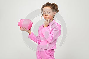 Finance. portrait of a thinking girl in a pink suit holding a money jar on a white background with copy space