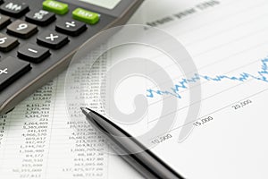Finance or stock market investment concept, pen on financial data report paper with pricing graph, chart and calculator