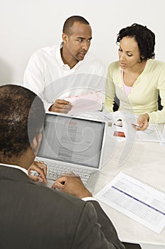 Financial Advisor Using Laptop With Couple In Discussion Over Documents