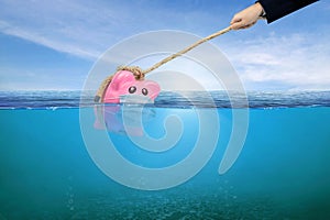 Financial Aid and rescue from debt problems for investments above water as a drowning pink piggy bank sinking in blue water
