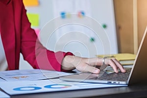 Financial, Asian businesswoman in red suit holding cup of coffee sitting on desk in office, having computer for doing accounting