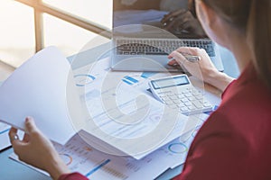 Financial, Asian businesswoman in red suit holding cup of coffee sitting on desk in office, having computer for doing accounting