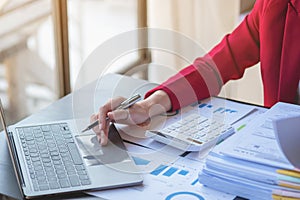 Financial, Asian businesswoman in red suit holding cup of coffee sitting on desk in office, having computer for doing accounting