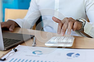 A financial businessman, a young man analyzes financial data using a computer and calculator to compute and summarize