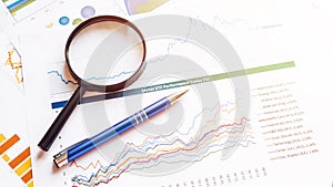 Financial chart on papers with magnifying glass and pen. Business accounting documents with finance marketing graphs